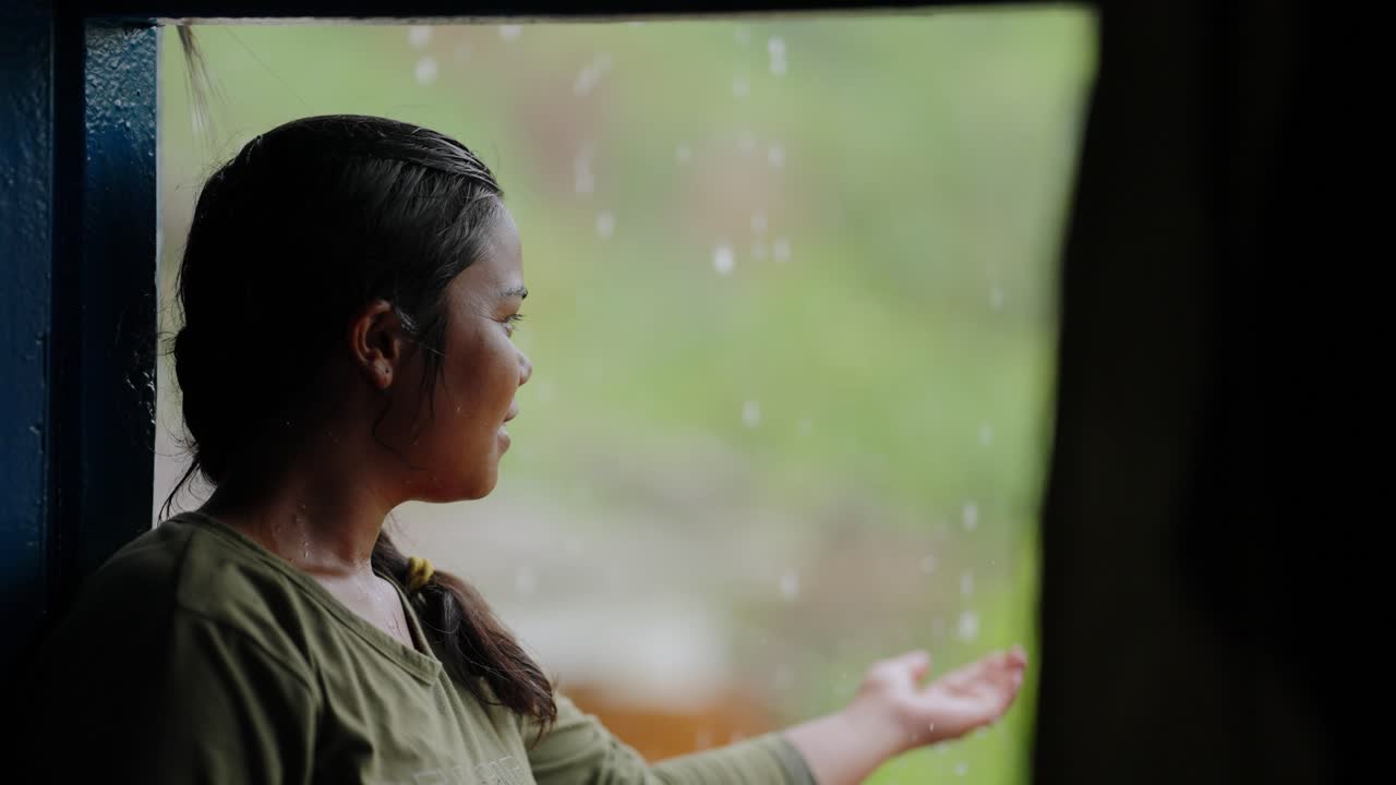 Indian village girl sitting at the doorstep of her house, smiling peacefully as she watches the rain, 4k video