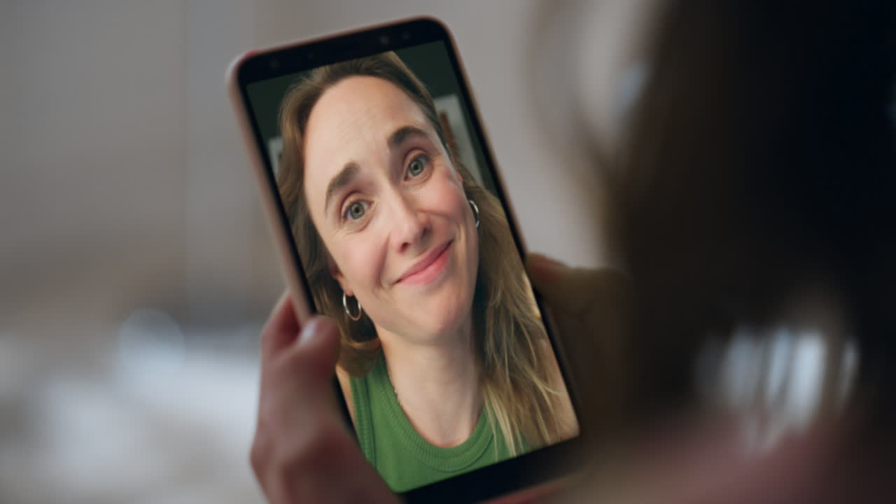 Glade kolleger på videoopkald på mobiltelefon. Hænder holder mobil