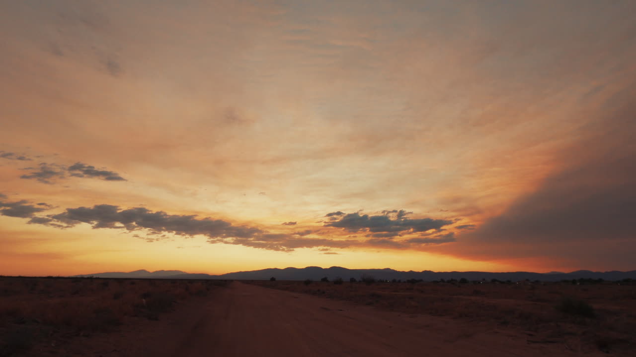 mirando a lo largo de un camino de tierra hacia el oeste mientras el sol se pone sobre el paisaje del desierto de mojave - lapso de tiempo estático