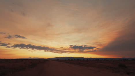 Mirando-A-Lo-Largo-De-Un-Camino-De-Tierra-Hacia-El-Oeste-Mientras-El-Sol-Se-Pone-Sobre-El-Paisaje-Del-Desierto-De-Mojave---Lapso-De-Tiempo-Estático