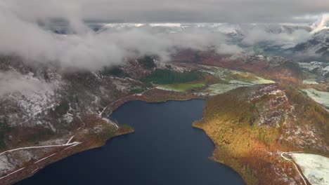 dark lake and mountains with light snow and patch of early morning sunshine on woodland tree hillside