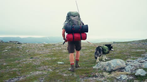 active man with backpack and dog trekking over misty mountain