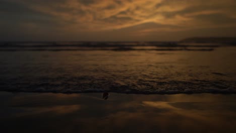 Strand-Mit-Grauem-Und-Goldenem-Himmel,-Der-Sich-In-Der-Abenddämmerung-Auf-Sand-Spiegelt,-Und-Wellen,-Die-Ruhig-An-Der-Küste-Zusammenbrechen