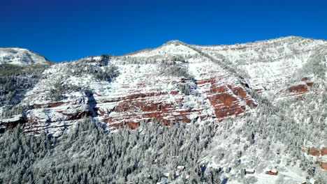 drone footage flying towards a giant red rock cliff covered in snow located in the rocky mountains of colorado