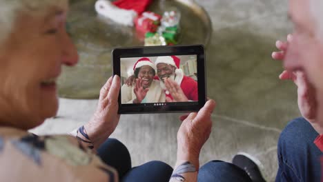 senior caucasian couple using tablet for christmas video call with happy couple on screen