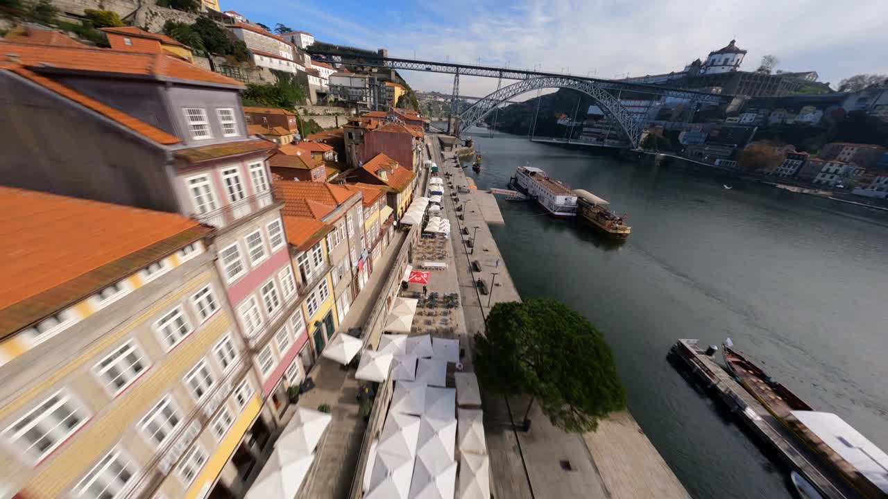 Telhados vermelhos passando rapidamente sobre a margem do rio, com drone FPV na Ponte Dom Luís, Porto, Portugal