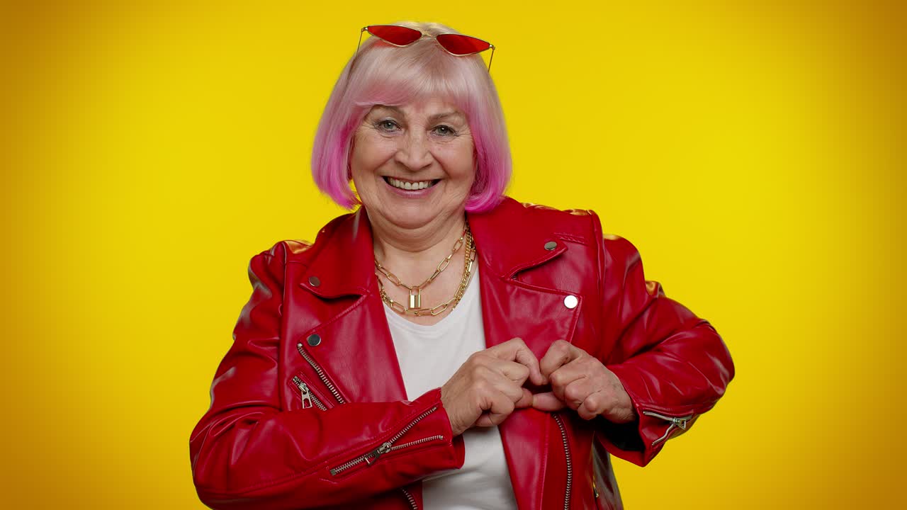 Una donna anziana sorridente fa un gesto del cuore, dimostra il segno dell'amore, esprime buoni sentimenti e simpatia.