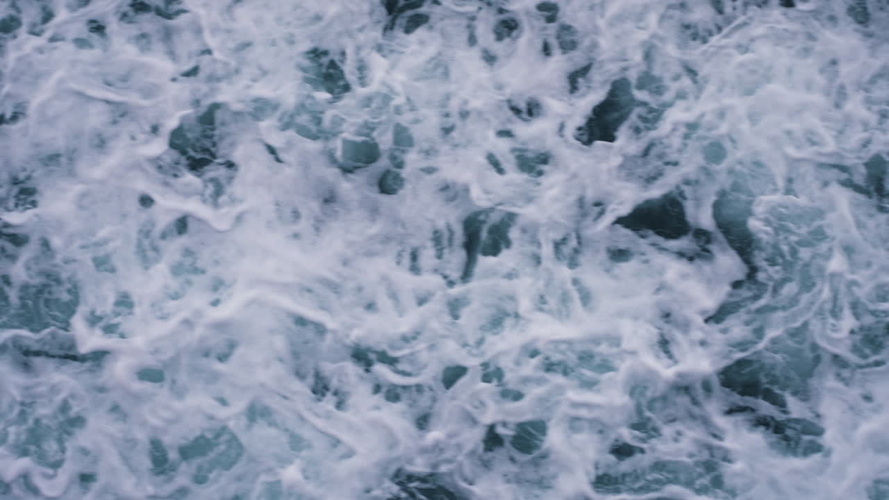 Slow motion top-down shot of waves crashing along the beach creating patterns
