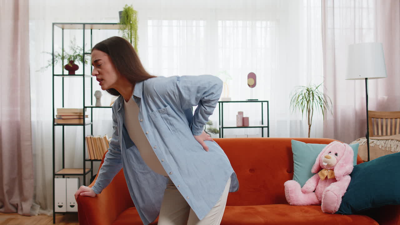 Upset ill young pregnant woman feeling sick suffering from lower back pain sitting on home sofa