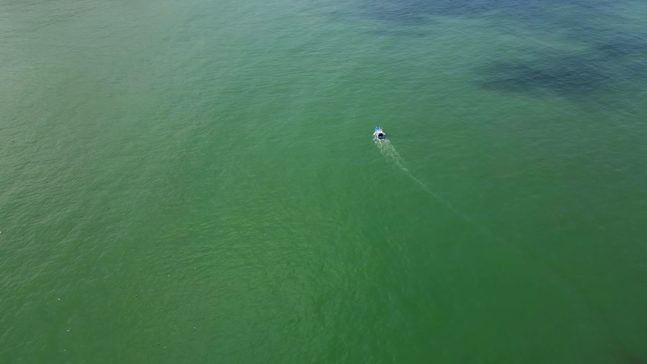 Cinematic drone opener following lone fishing boat on ocean, tilt up shot