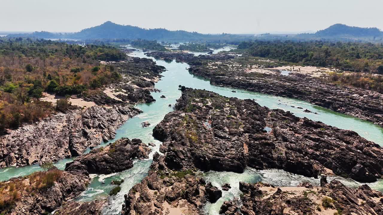 Drone glides slowly above the jagged rock formations and powerful rapids of the Mekong River near Don Det in the Si Phan Don region of Laos, revealing a dramatic and untamed tropical river landscape