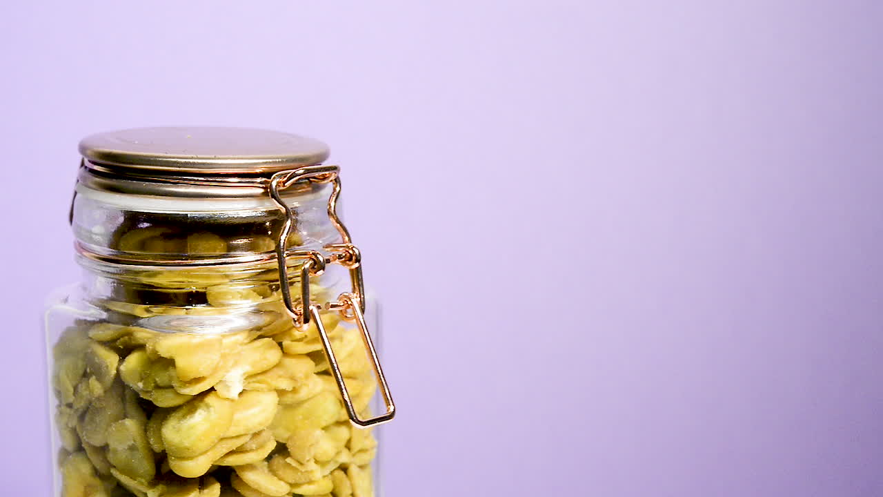 primer plano de un tarro de albañil hermético que gira con habas tostadas sobre un fondo lila neón