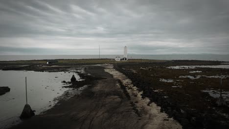 aerial-beach-footpath-leading-to-lighhouse-on-grotta-island,-reykjavik-iceland,-dark-cloudy-moody-scenery,-flying-up