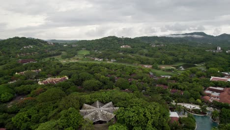 a flyover drone shot over a resort and golf course, having unique central-american style buildings and rooftops, surrounded by dense jungle, in northern costa rica