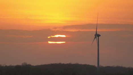 pittoresco del sole che si nasconde dietro le nuvole nel cielo arancione durante il tramonto con un mulino a vento isolato in primo piano