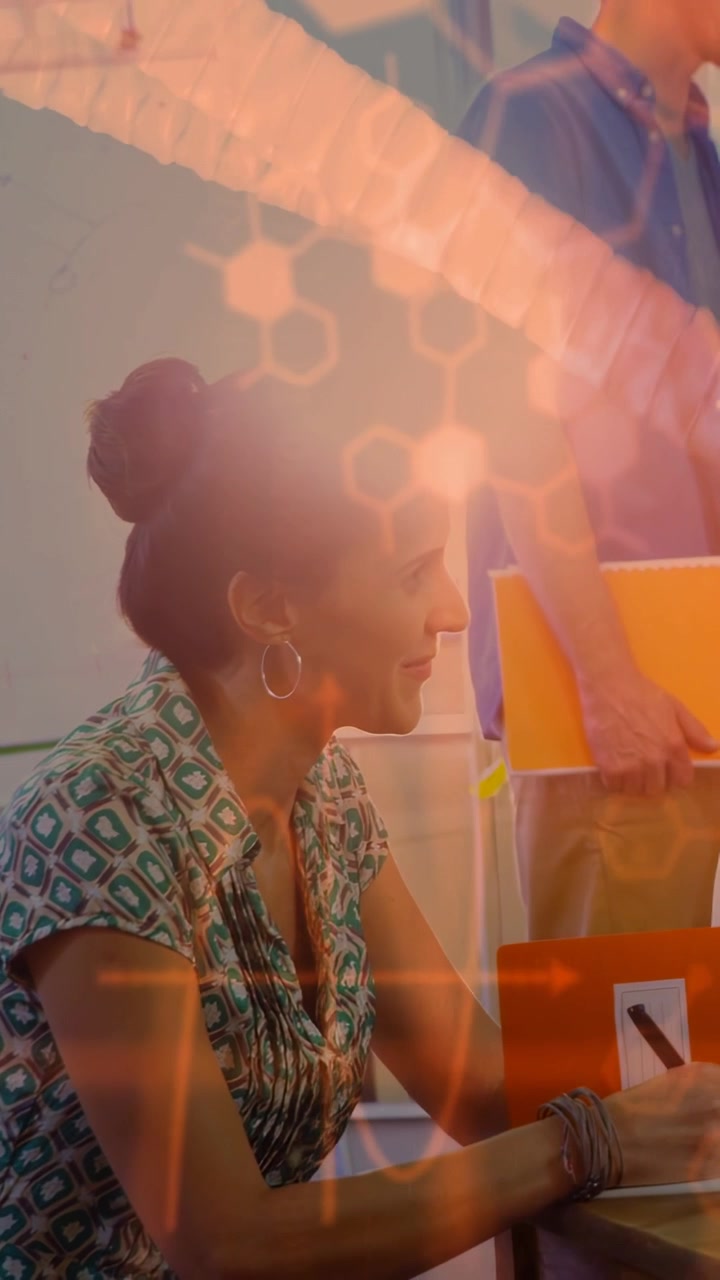 Vertical video: Woman noting for biz plans as peer coming with orange folder, hex overlay on notes