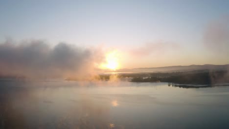 sunrise at a lake, flying through a mist floating over a water surface