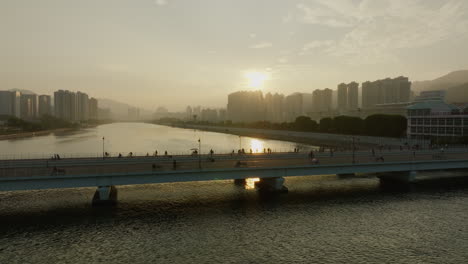 pedestrian walking and cycling on hong kong bridge at sunset with scenic cityscape skyline in background aerial cinematic footage