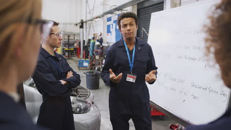 Männlicher-Nachhilfelehrer-Am-Whiteboard-Mit-Studenten,-Die-An-Der-Hochschule-Eine-Kfz-Mechaniker-Ausbildung-Unterrichten