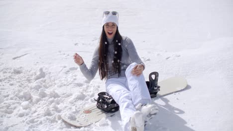 Atractiva-Mujer-Joven-Sentada-En-Su-Tabla-De-Snowboard