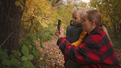 madre está enseñando a su hijo pequeño a tomar fotos con el teléfono inteligente un viaje familiar a la naturaleza en el bosque de otoño o parque infancia y maternidad