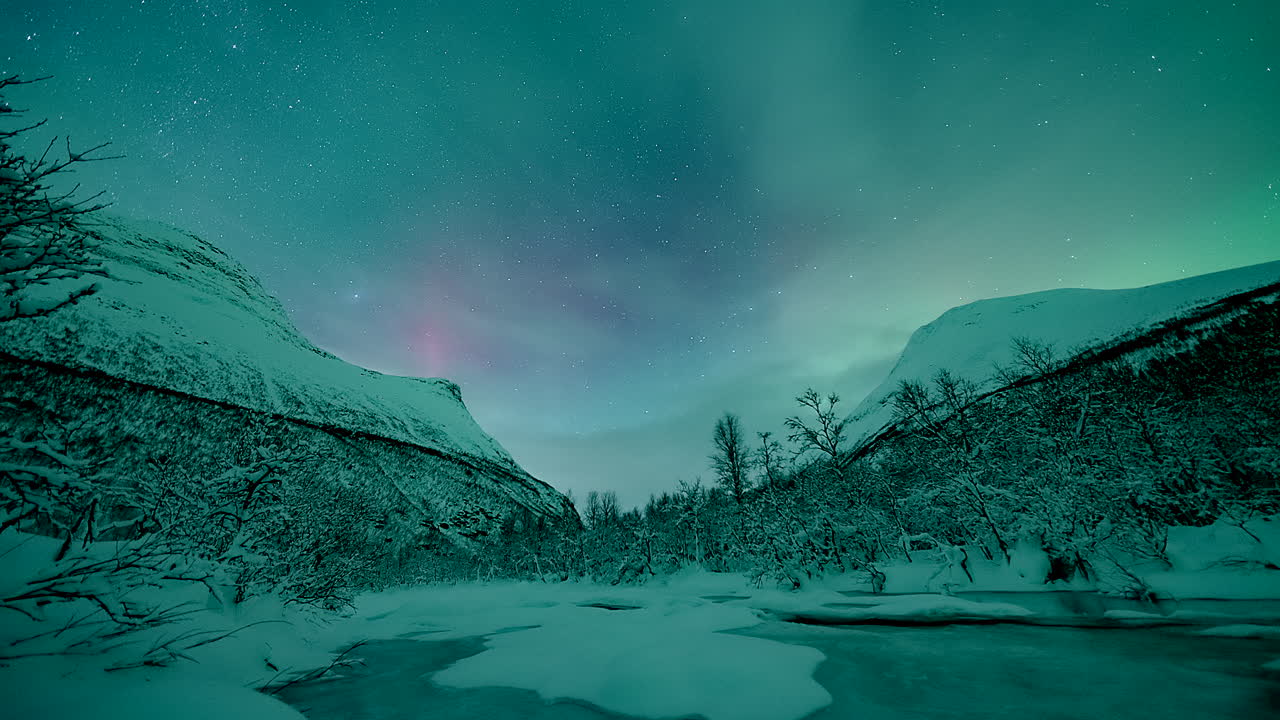 Timelapse di aurore boreali nel cielo stellato sopra un fiume ghiacciato e montagne innevate