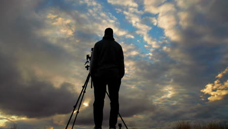 Silhouette-photographer-with-checking-camera-on-tripod-with-cloudy-sky
