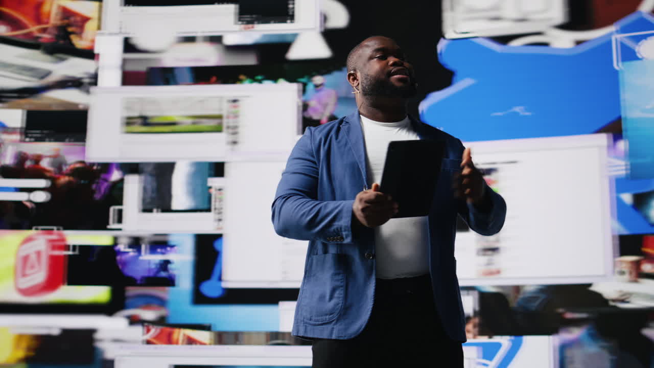 Black presenter hosting conference on stage surrounded by media visuals