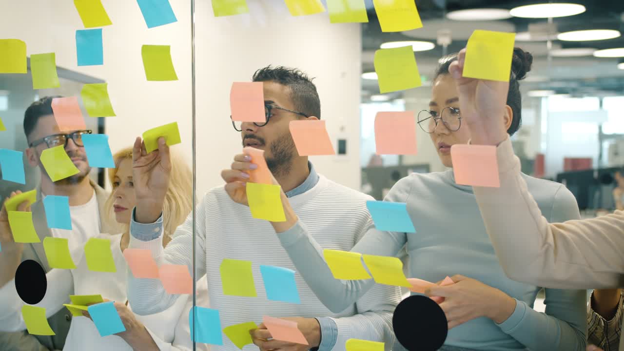 Slow motion of multi-ethnic team sticking colorful notes on glass board in office