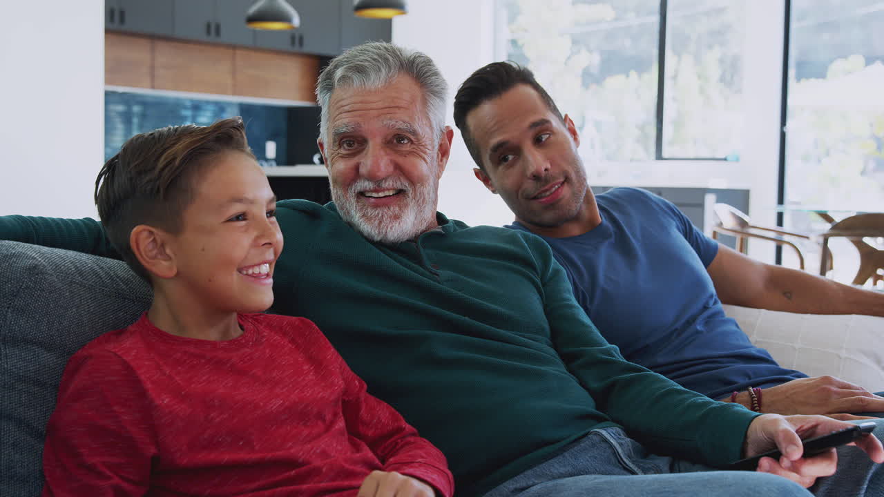 Hispanic familie med flere generationer sidder på sofaen derhjemme og ser film sammen