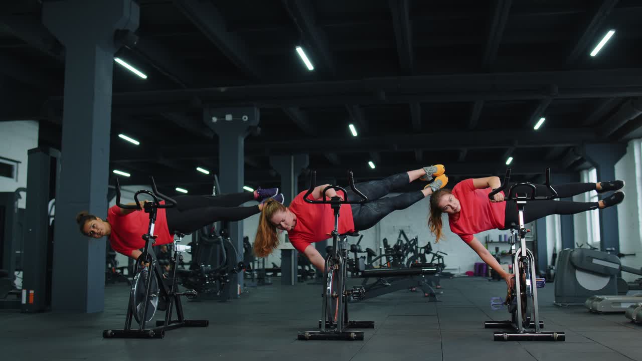 Athletic women group training tricks on spinning stationary bike routine in gym weight loss indoors