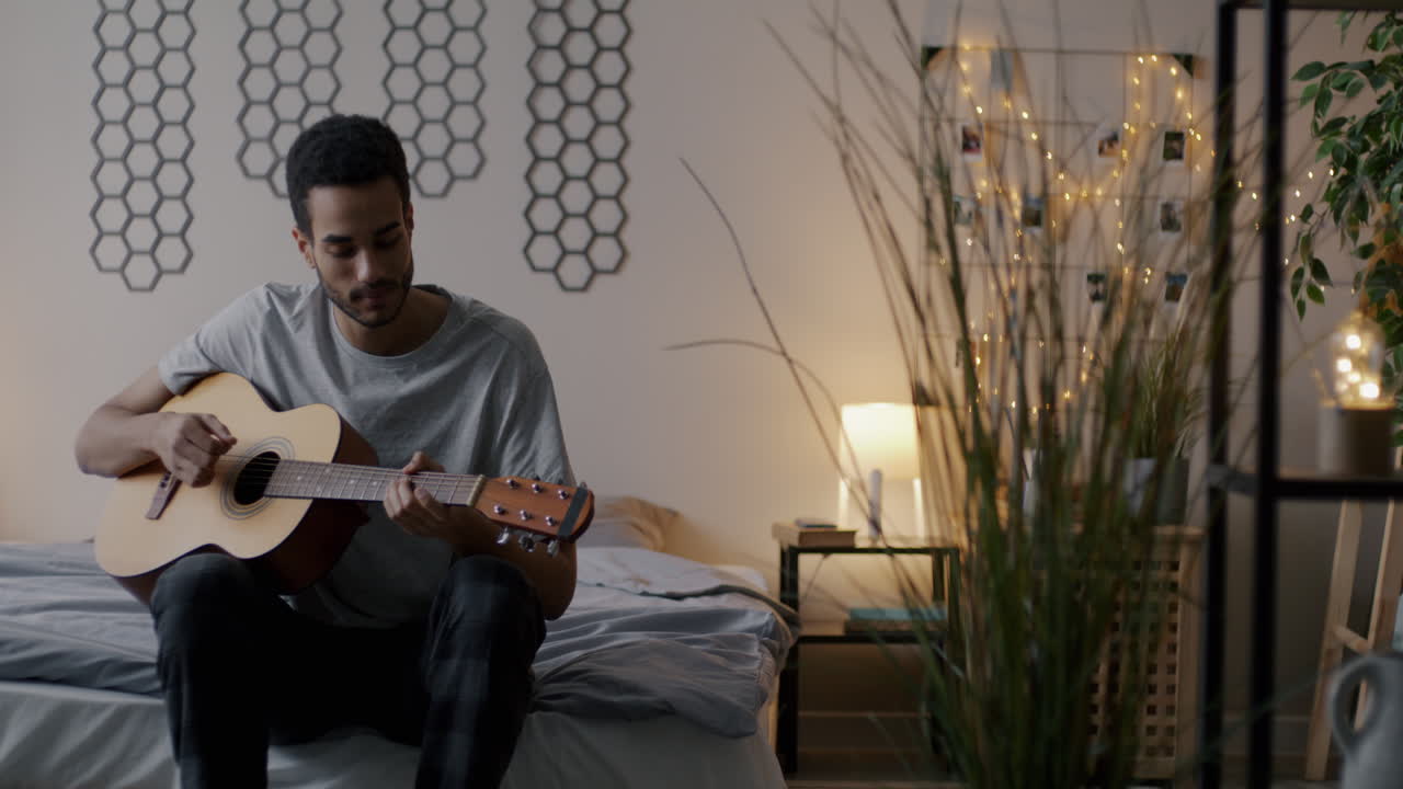 Mand spiller akustisk guitar på sit soveværelse