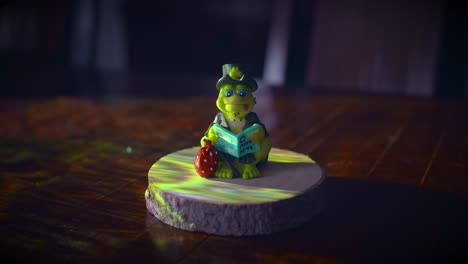 ceramic frog reading newspaper, sitting on wooden presentation base against spotlight