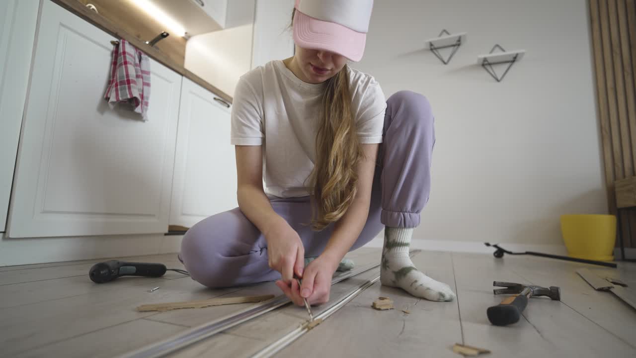 Woman struggles while trying to fix a floor transition strip at home, capturing DIY challenge, problem solving, and home improvement effort with tools on the floor