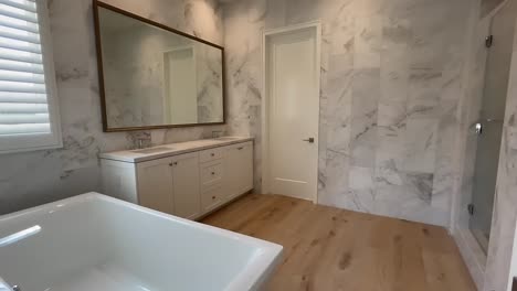 baño principal moderno con paredes de mármol y suelos de madera