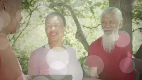 animation of spots of light and trees over diverse senior people talking in garden