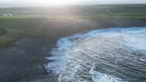 Sunrise-with-waves-crashing-against-the-shore,-warm-light-accentuating-the-rugged-landscape