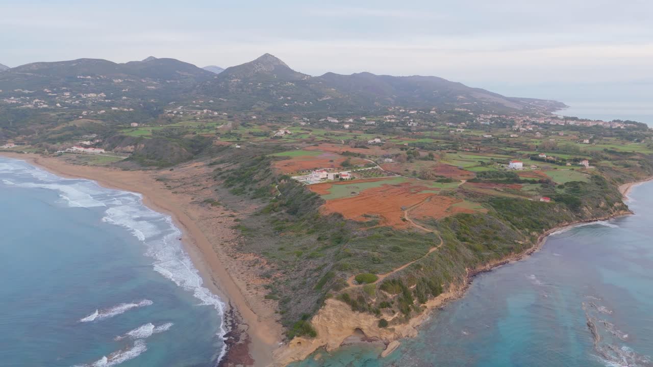 Sweeping drone shot of southern Kefalonia near Skala, capturing coastline, farmlands, and mountains under soft light.