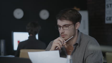 Concentrated-business-analyst-watching-document-and-laptop-screen-in-dark-office