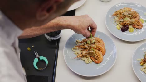 Chef-Masculino-Caucásico-Vistiendo-Chefs-Blancos-En-La-Cocina-De-Un-Restaurante,-Poniendo-Comida-En-Un-Plato