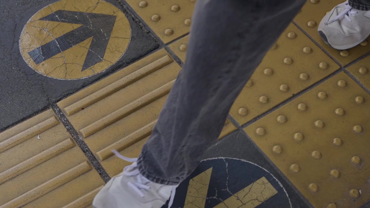 Person in sneakers walking over yellow tactile paving with arrows at station Japan
