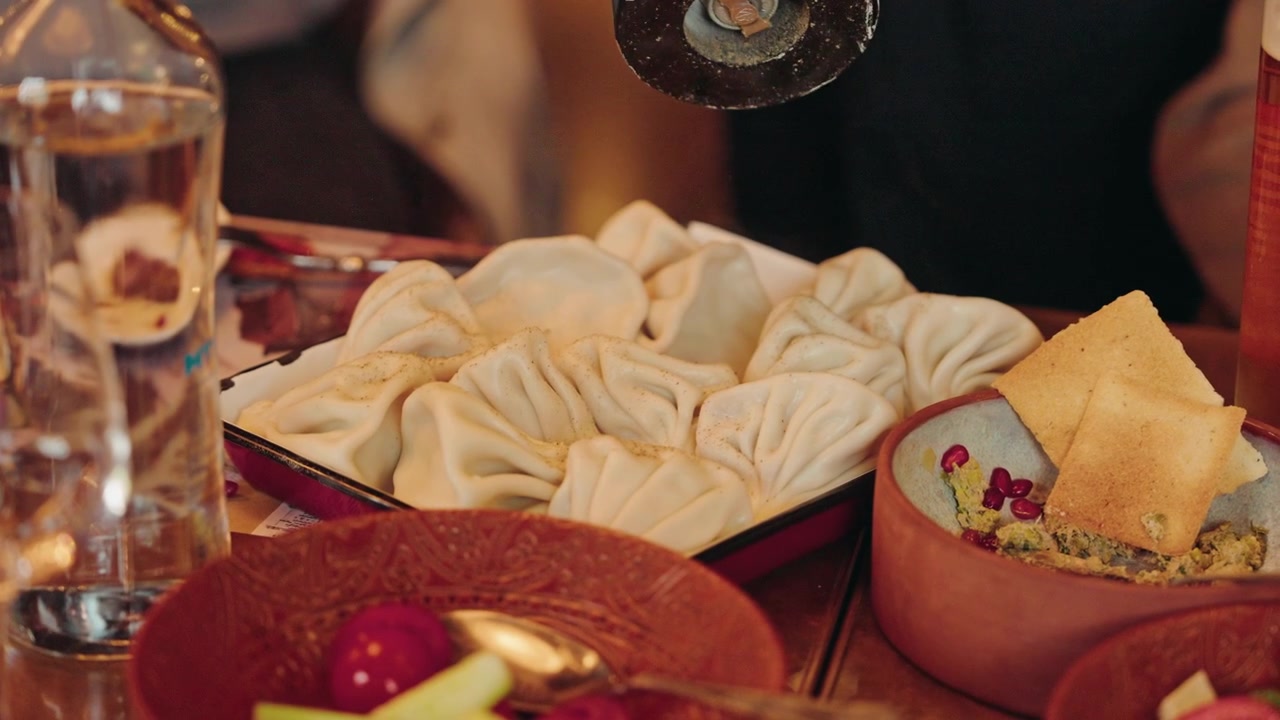 A plate of Georgian khinkali dumplings with pkhali and lavash on a laid restaurant table.