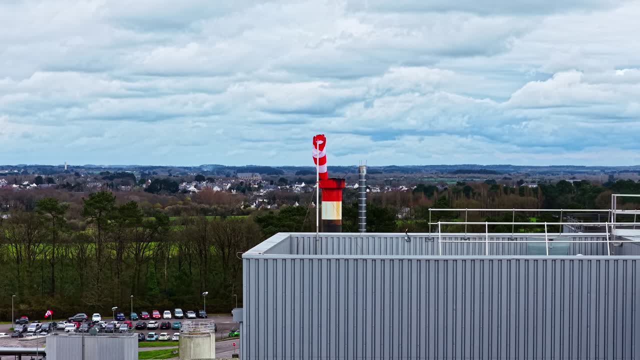 Luchtfoto van een fabrieksdak met een rood-wit gestreepte windzak die de windrichting aangeeft.