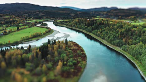 the landscape is a blend of vibrant farm fields and autumn forests, with a winding river leading the eye toward the mountains