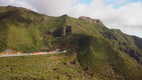 Highway-leading-to-tunnel-through-a-big-mountain,-green-landscape-scenery