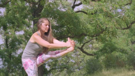 Mujer-Joven-Haciendo-Yoga-Estirar-La-Pierna-En-Un-Entorno-Tipo-Madera-O-Parque