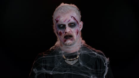 unheimlicher mann mit schrecklichem halloween-toten-zombie-make-up in einem kostüm, der für die kamera ominös aussieht