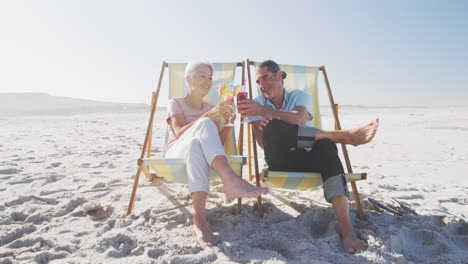 senior caucasian couple sitting on sunbeds at the beach.