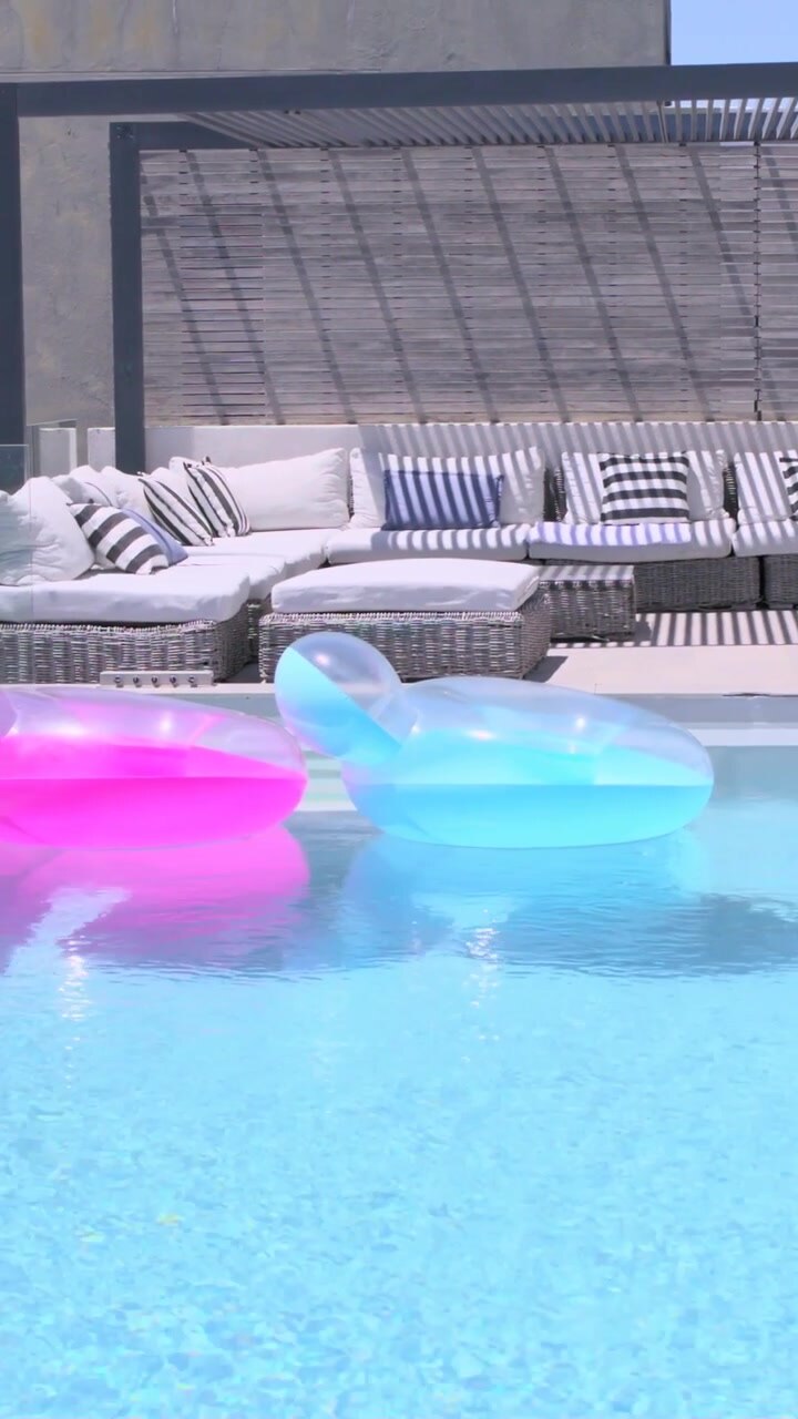 Vertical video: Drifting with breeze, bright pink float moving to terrace pool, passing blue float
