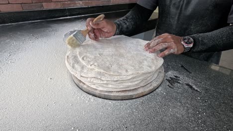 skilled hands preparing and dusting flatbread dough.